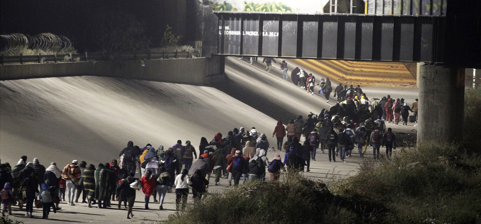 Migrantes corren a lo largo de las orillas del Río Grande hacia una puerta en el muro fronterizo donde algunos ingresaron a Estados Unidos para solicitar asilo, el martes 20 de diciembre de 2022 en El Paso, Texas. (Foto AP/Morgan Lee)