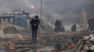 Un manifestante corre mientras la policía antidisturbios se mantiene fuera del Parlamento durante una protesta en el centro de Atenas, Grecia, para conmemorar los dos años del mortal desastre ferroviario que también desencadenó cientos de otras manifestaciones y una huelga general, el viernes 28 de febrero de 2025. (Foto AP/Petros Giannakouris)