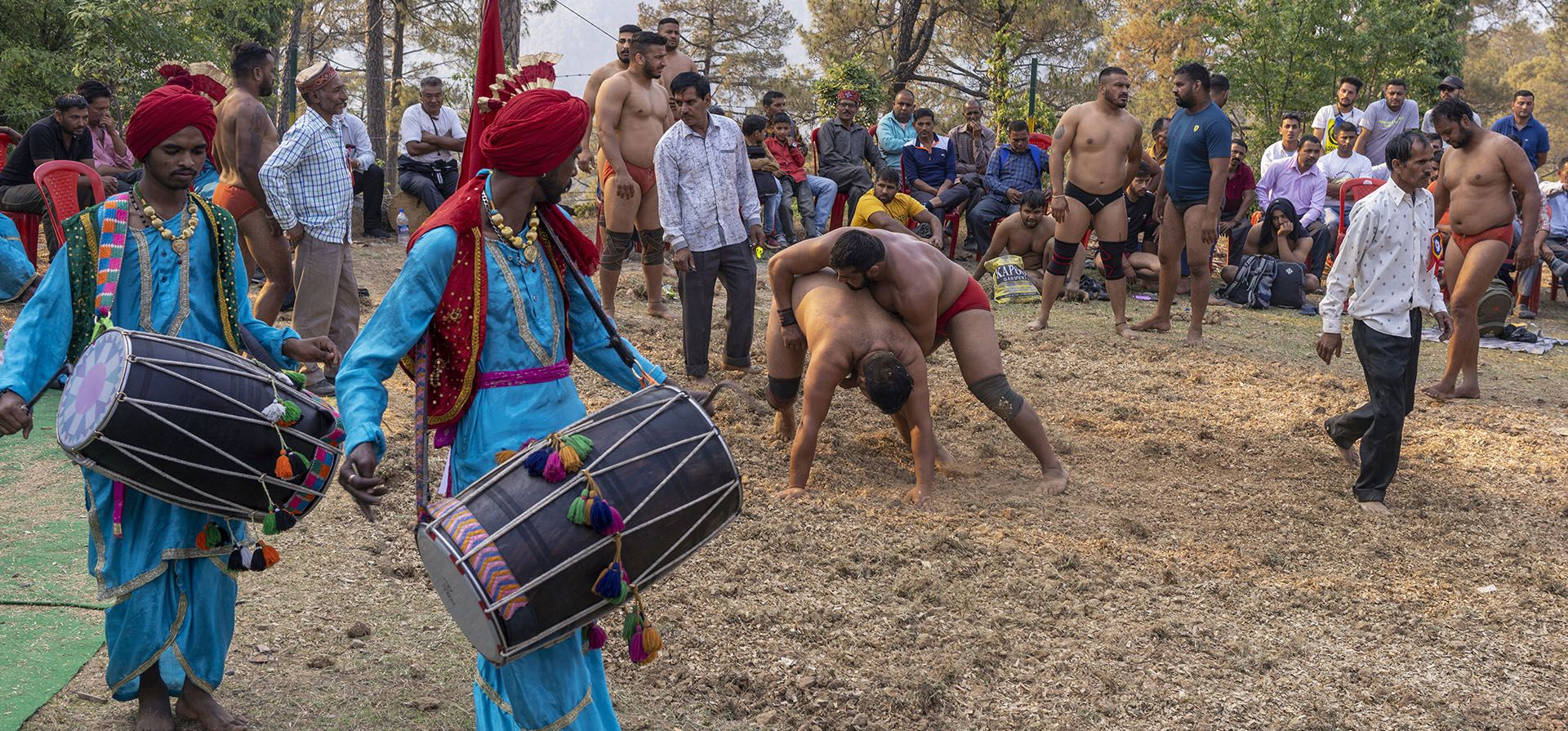 Tamborileros con atuendos tradicionales dan vueltas alrededor de un cuadrilátero de arena mientras los luchadores compiten en una feria en la aldea de Satovari, Dharmsala, India, el domingo 24 de abril de 2022. Luchadores aspirantes y experimentados compiten en estas ferias por recompensas monetarias.