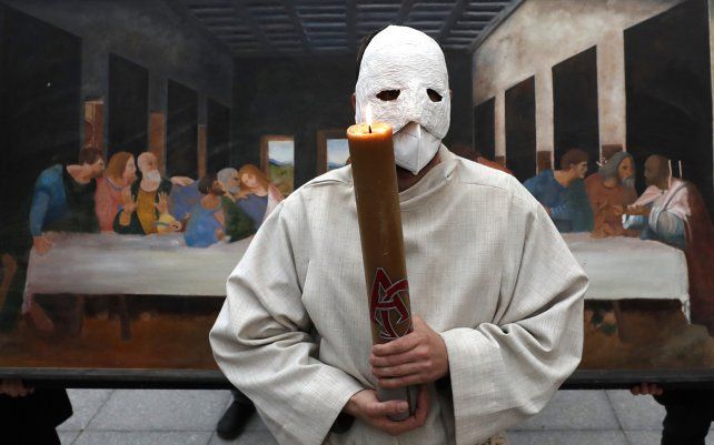 Un participante con una máscara sostiene una vela mientras se para frente a una representación de la pintura de la Última Cena durante una procesión de Pascua que marcha por las calles de Ceske Budejovice, República Checa.