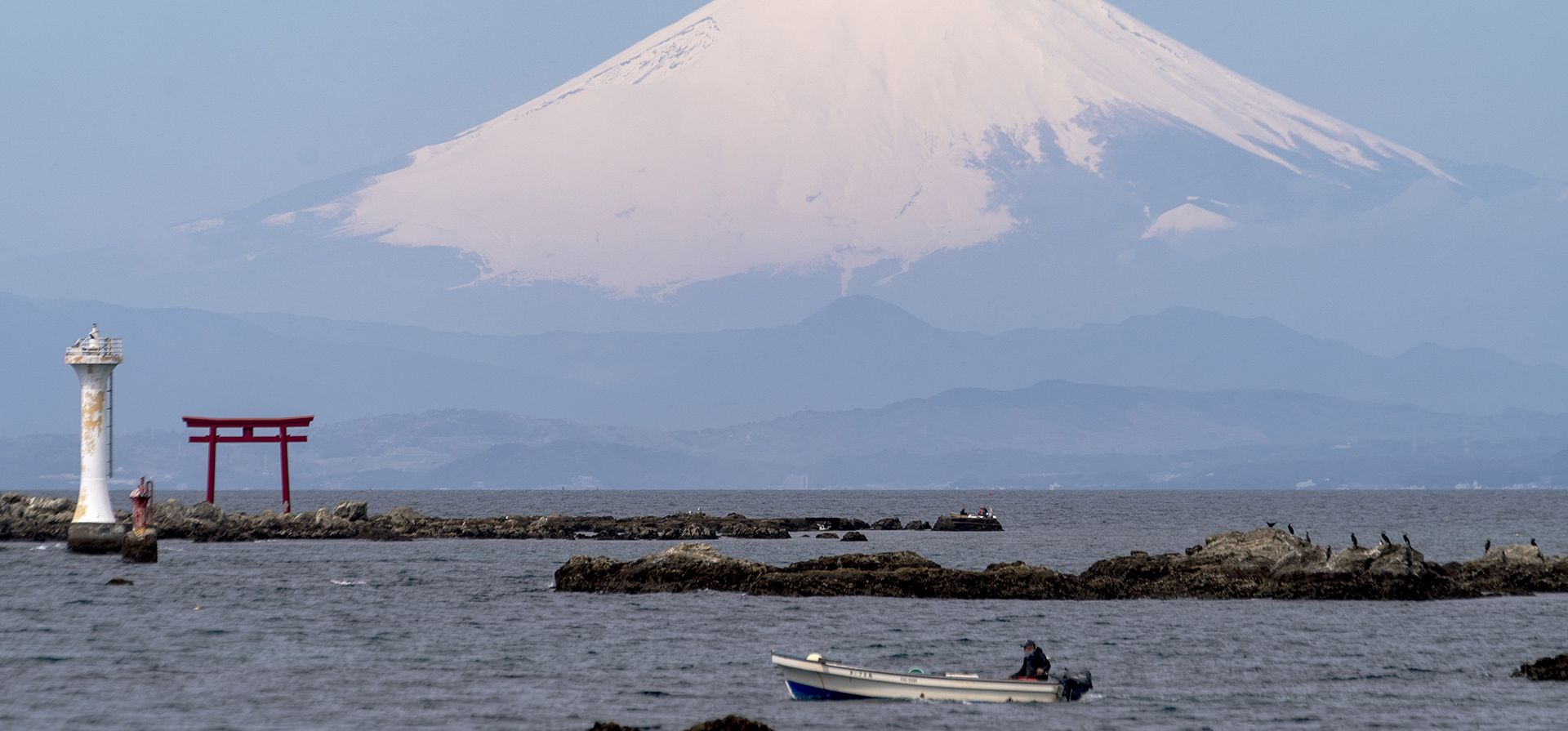 Con el monte Fuji al fondo, un barco de pesca navega cerca de una puerta Torii, puerta de entrada a un santuario sintoísta, en la bahía de Sagami el miércoles 6 de abril de 2022 en Zushi, al sur de Tokio.