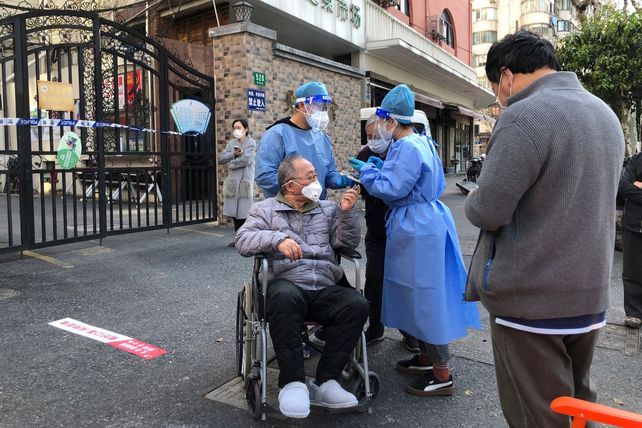 Agentes sanitarios terminan de testear en plena calle a un hombre en silla de ruedas en un distrito de Shanghái.