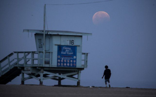Una mujer observa cómo la luna llena se pone sobre la playa de Santa Mónica en California, el miércoles 26 de mayo de 2021. El primer eclipse lunar total en más de dos años coincide con una superluna de un espectáculo cósmico.