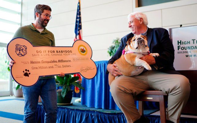 El último ganador de un millón de dólares en el sorteo de vacunación de West Virginia, posa con el gobernador, Jim Justice. El gobernador estuvo acompañado por su mascota Bulldog Inglés, Babydog, que es la mascota del sorteo de vacunación “Do it for Babydog”