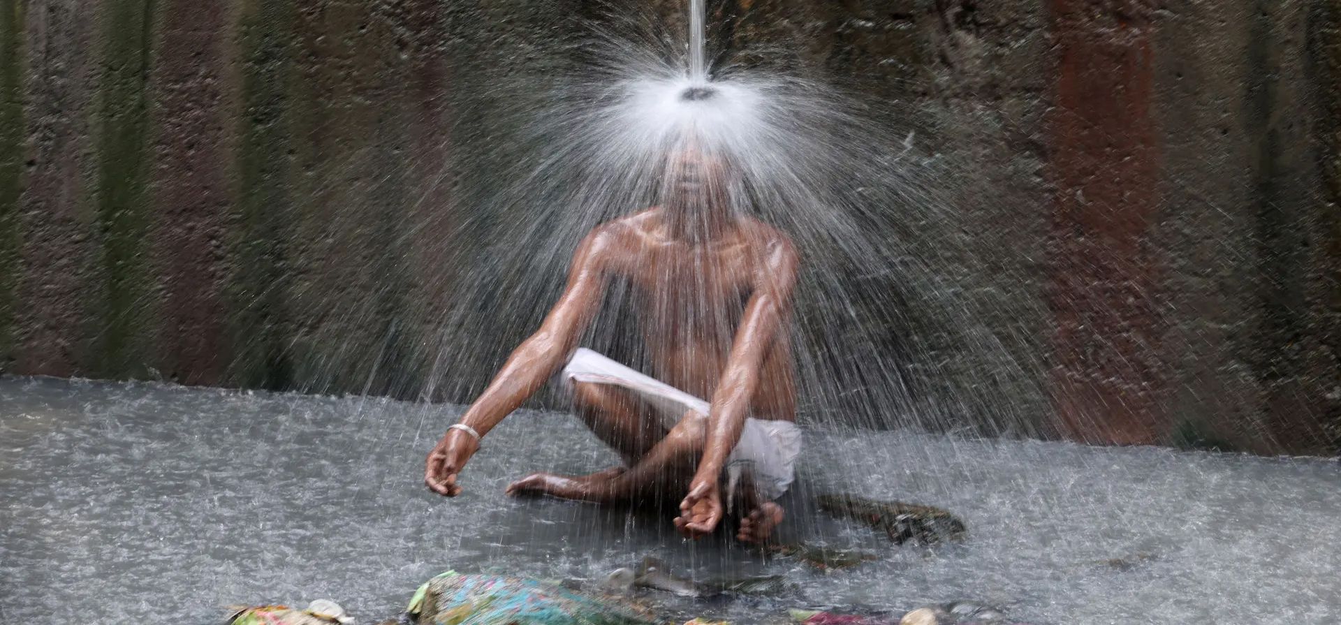 Un hombre se enfría bajo una tubería de agua que fluye en una calle de Nueva Delhi, India. Fotografía: Anushree Fadnavis/Reuters