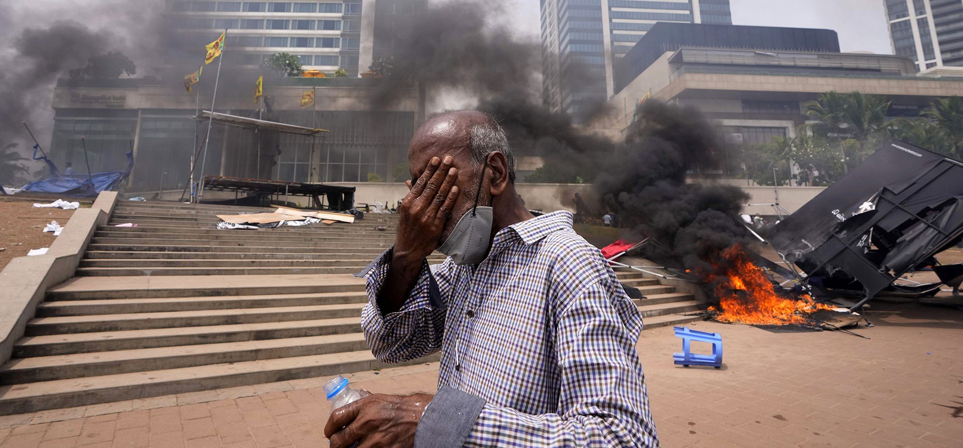 Un hombre de Sri Lanka reacciona a los gases lacrimógenos mientras camina frente al lugar destrozado de las protestas antigubernamentales frente a la oficina del presidente en Colombo, Sri Lanka, el lunes 9 de mayo de 2022.