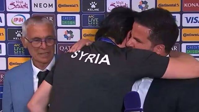 Héctor Cúper observa el abrazo de su traductor con el periodista tras la victoria de Siria.