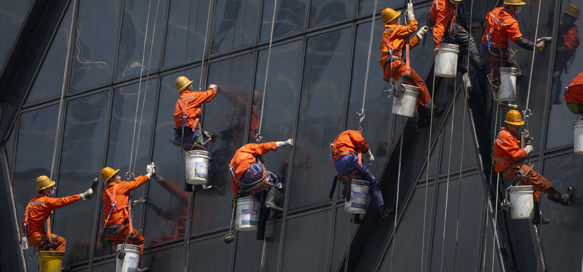 Trabajadores cuelgan de cuerdas mientras lavan ventanas en el edificio de la Televisión Central de China (CCTV) en Beijing, el miércoles 4 de mayo de 2022. Beijing cerró el miércoles alrededor del 10% de las estaciones de su vasto sistema de metro como medida adicional contra la propagación del coronavirus.