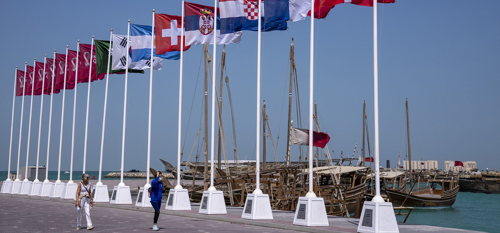 Turistas caminan junto a las banderas de algunos de los países clasificados en el paseo marítimo de Doha, Qatar, el martes 29 de marzo de 2022. El sorteo de la Copa del Mundo de fútbol se realizará en Doha el viernes 1 de abril.