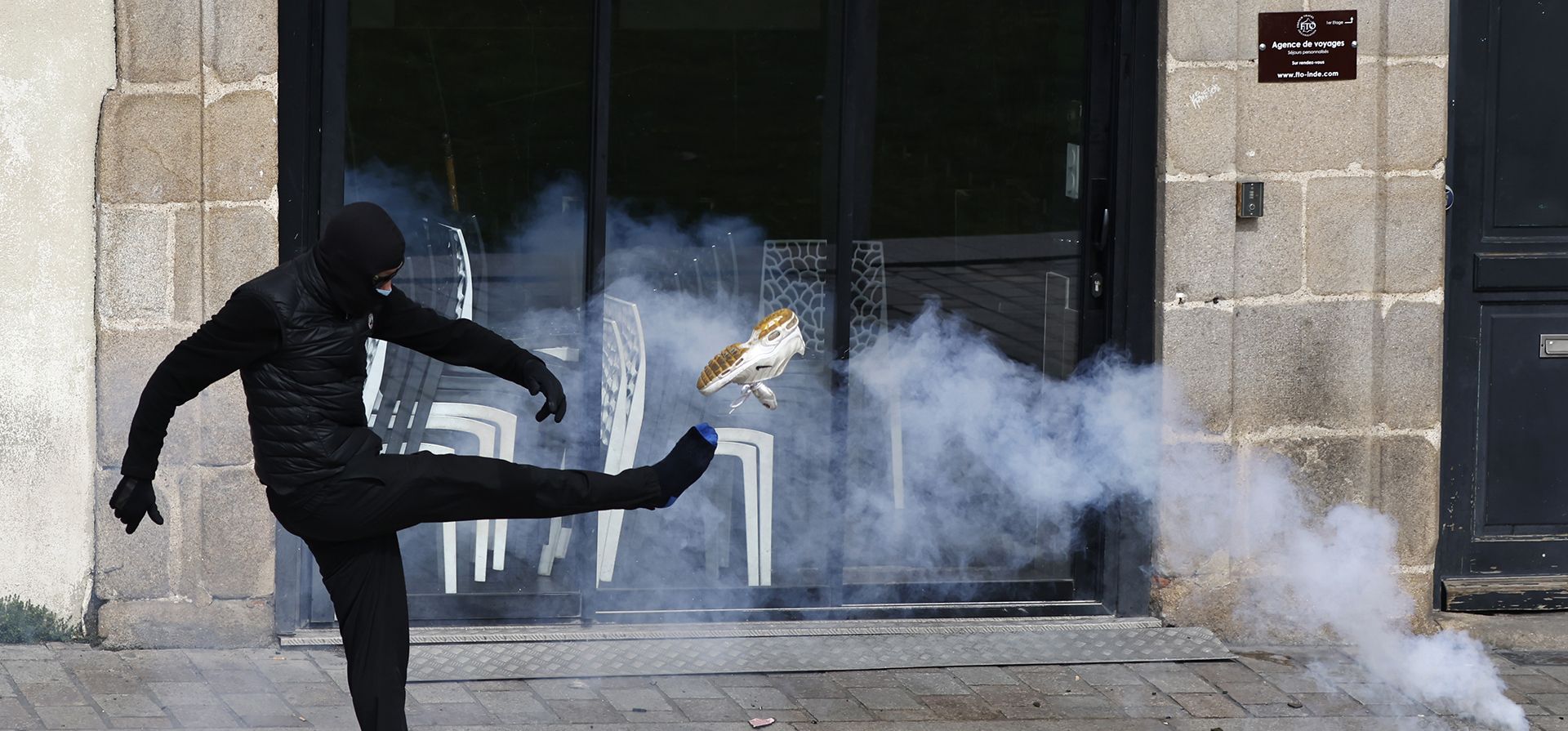 Un joven pierde su zapatilla al patear un bote de gas lacrimógeno durante una manifestación contra el plan del presidente Macron de retrasar la edad legal de jubilación de Francia de 62 a 64 años, en Nantes, oeste de Francia, el martes 28 de marzo de 2023. (Foto AP/Jeremias Gonzalez )