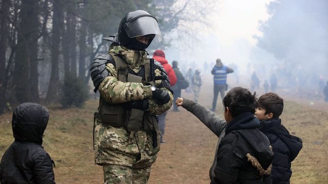 Un militar bielorruso saluda a los niños migrantes de Oriente Medio y otros lugares reunidos en la frontera entre Bielorrusia y Polonia cerca de Grodno, Bielorrusia, el miércoles 10 de noviembre de 2021. El gobierno alemán dice que la canciller Angela Merkel ha pedido al presidente ruso Vladimir Putin que intervenga con Bielorrusia la situación de los migrantes en la frontera de ese país con Polonia.