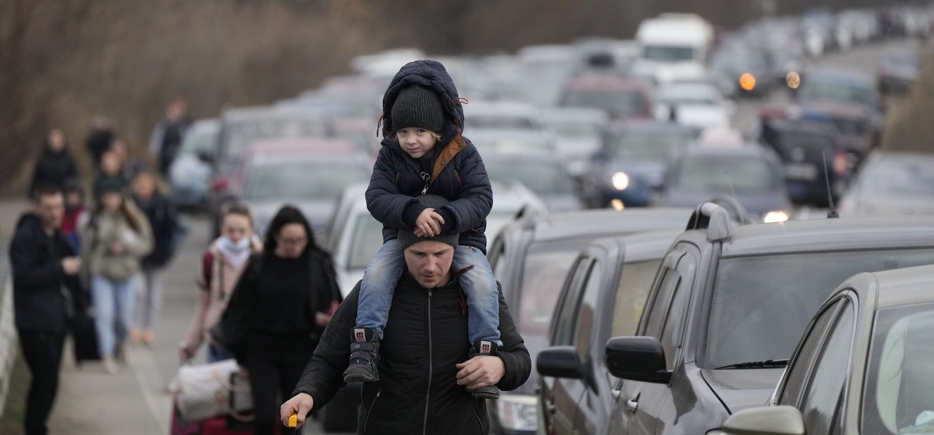 Refugiados ucranianos caminan junto a vehículos que hacen fila para cruzar la frontera de Ucrania a Moldavia, en el cruce fronterizo de Mayaky-Udobne cerca de Udobne, Ucrania. La agencia de refugiados de la ONU dice que más de 870.000 personas han huido hasta ahora de Ucrania a los países vecinos tras la invasión rusa.
