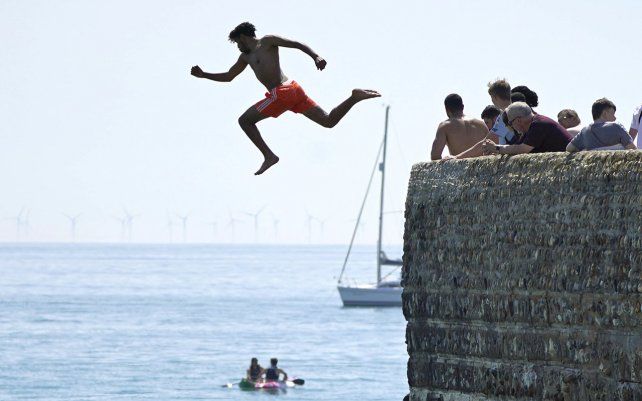 Un hombre salta al mar mientras la gente disfruta del sol en la playa de Brighton, al sureste de Inglaterra, el miércoles 16 de junio de 2021.
