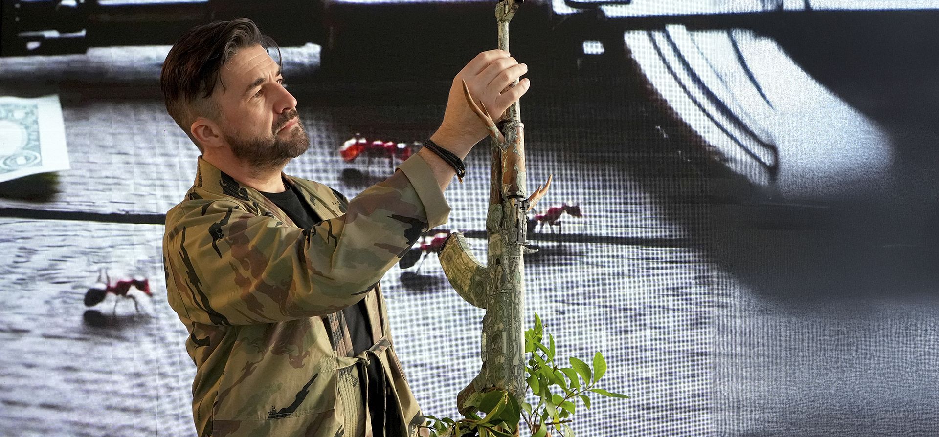 El artista británico y ex soldado de las Fuerzas Especiales, Bran, observa su obra de arte titulada The Colony (2025), en la que hormigas cortadoras de hojas transportan fragmentos de billetes de dólar a través de una escultura de AK-47, en exhibición en su exposición Art to Disarm 2025, en la galería HOFA, en Londres, el jueves 6 de febrero de 2025. (Foto AP/Kirsty Wigglesworth) El artista británico y ex soldado de las Fuerzas Especiales, Bran, observa su obra de arte titulada The Colony (2025), en la que hormigas cortadoras de hojas transportan fragmentos de billetes de dólar a través de una escultura de AK-47, en exhibición en su exposición Art to Disarm 2025, en la galería HOFA, en Londres, el jueves 6 de febrero de 2025. (Foto AP/Kirsty Wigglesworth)