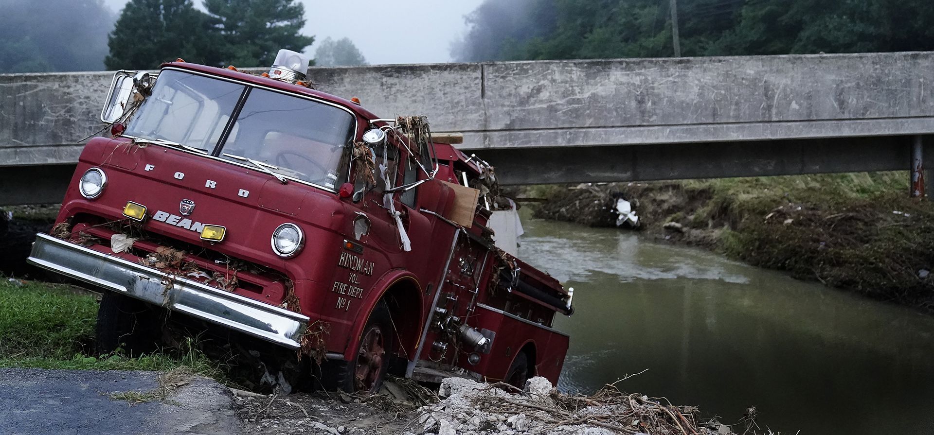 Un camión de bomberos colgando sobre el borde del agua, el miércoles, 3 de agosto de 2022, en Hindman, Kentucky., después de que una inundación masiva llevara el camión de bomberos hacia el agua. Las temperaturas se están disparando en una región del este de Kentucky donde la gente está sacando a pala los restos de las inundaciones masivas.