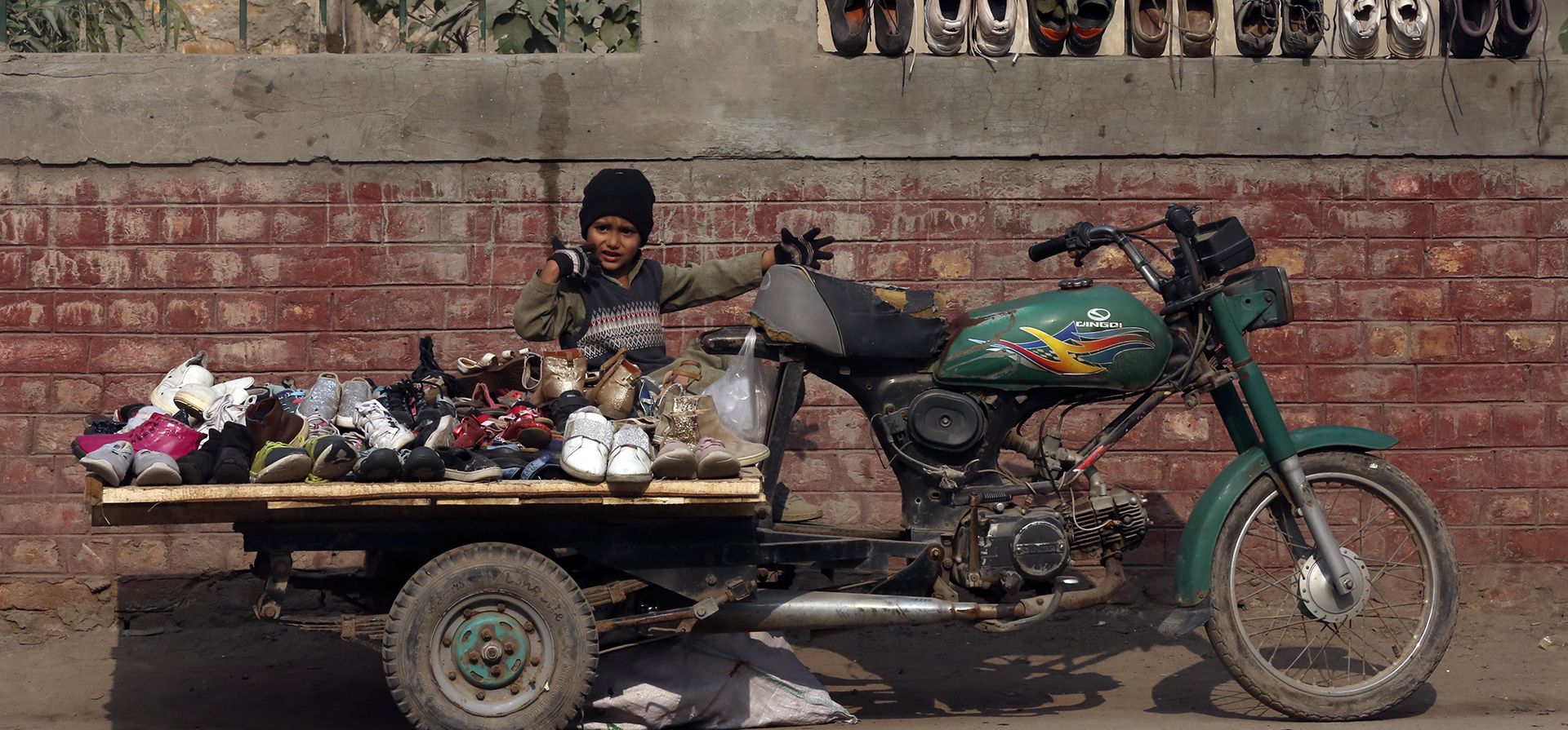 Un niño paquistaní que vende zapatos de segunda mano espera clientes en una calle de Peshawar, Pakistán, el lunes 5 de diciembre de 2022. (Foto AP/Muhammad Sajjad)