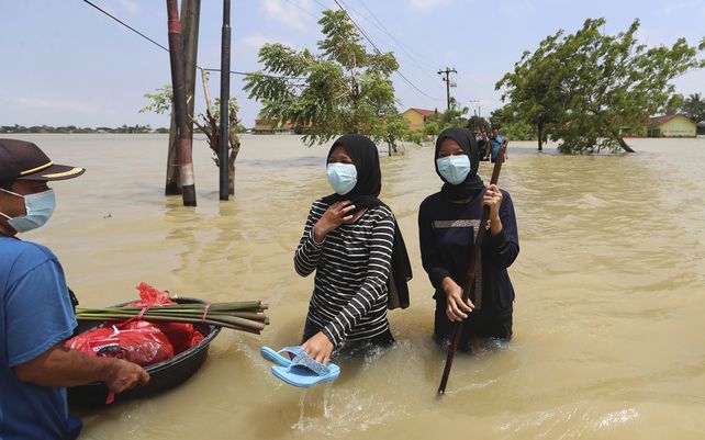 Jóvenes cargan sus pertenencias mientras caminan por el agua en un vecindario inundado luego de las fuertes lluvias en Bekasi