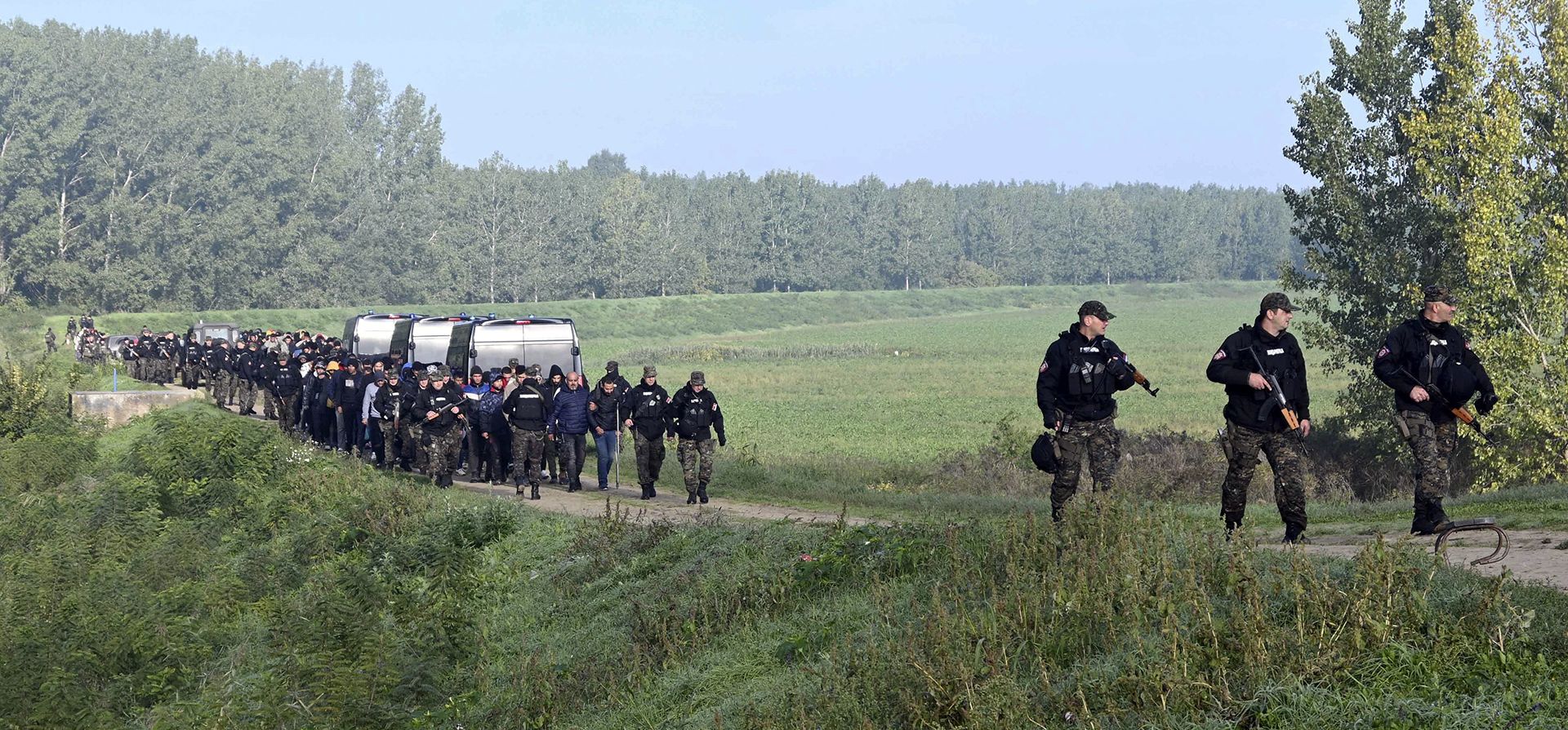 Agentes de la policía escoltan a migrantes cerca de la aldea de Srpski Kustur, en Serbia, el miércoles 5 de octubre de 2022. La policía serbia allanó el miércoles un campamento improvisado cerca de la frontera con Hungría, donde encontraron 200 migrantes, traficantes de personas detenidos y armas y dinero confiscados.