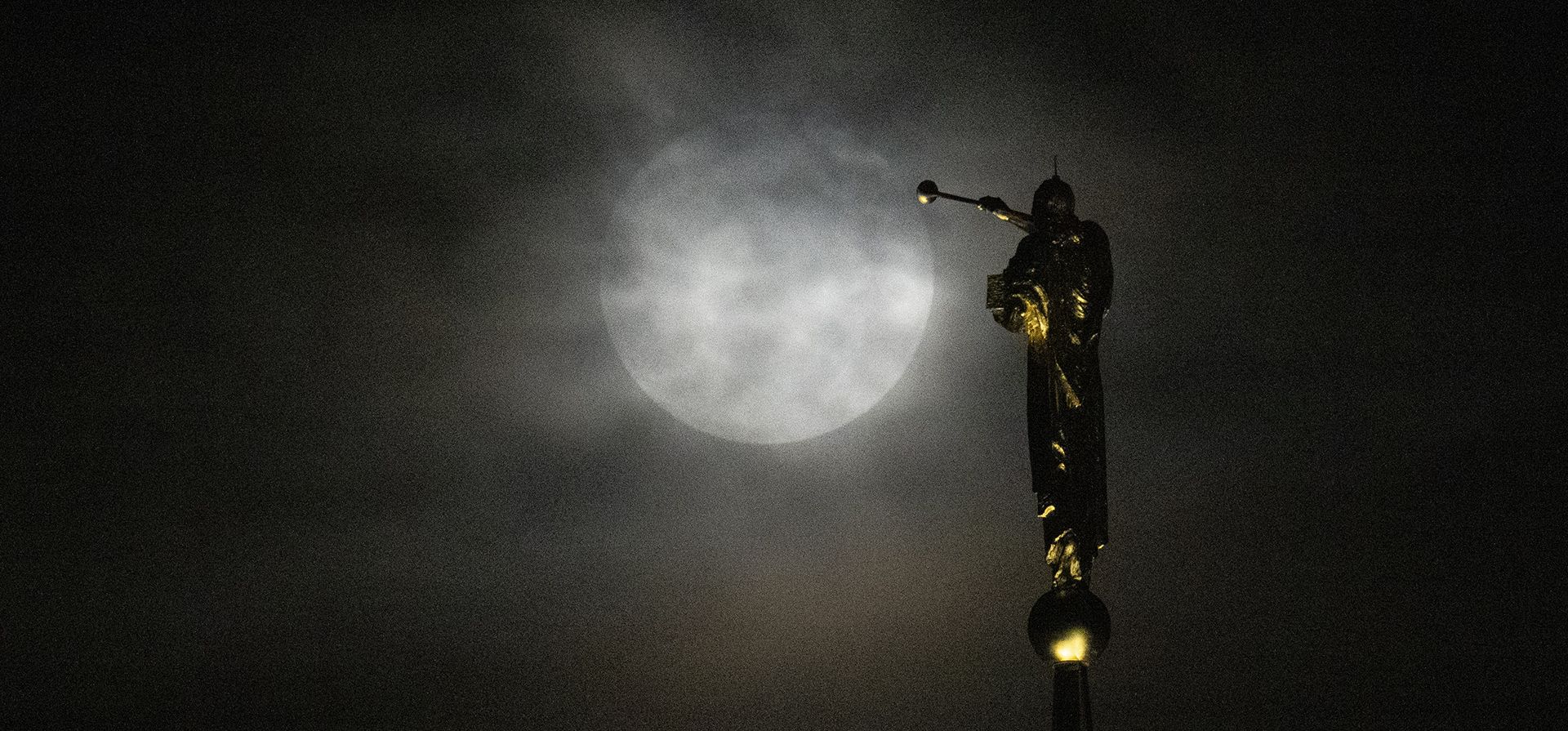 La superluna, la luna azul, se eleva detrás de una gruesa capa de nubes cerca de una estatua del ángel Moroni encaramada en lo alto de la Iglesia de Jesucristo de los Santos de los Últimos Días, el miércoles 30 de agosto de 2023, en Kensington, Maryland. (Foto AP/Julio Cortez)