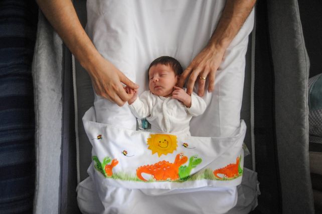Bautista duerme tranquilo en su cuna y de la mano de cada uno de sus padres.