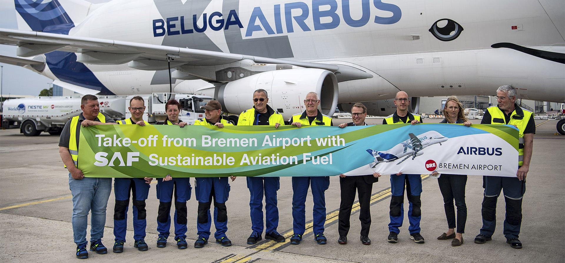 Empleados de Airbus y del aeropuerto de Bremen se paran con una pancarta frente al avión de transporte de fuselaje ancho de Airbus del tipo Beluga XL, que se llenó con el combustible "Combustible de aviación sostenible" (SAF) por primera vez en Bremen, Alemania, el martes. , 10 de mayo de 2022.