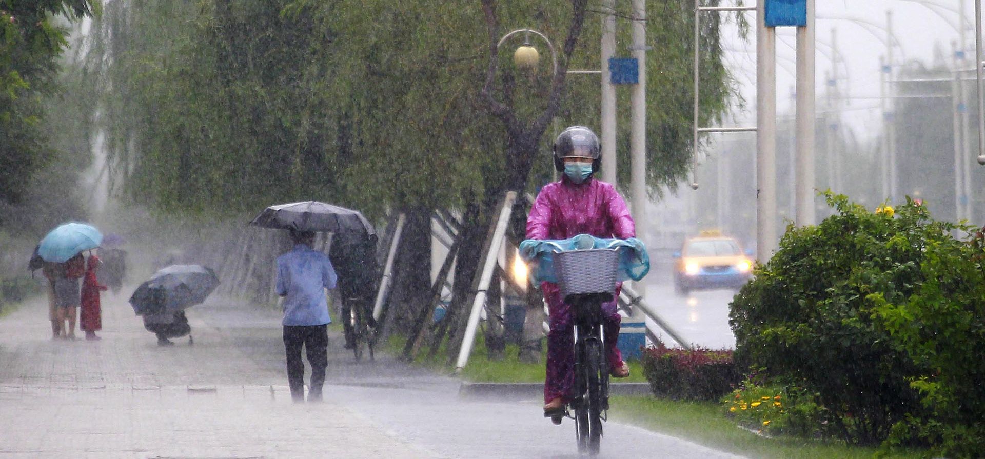 Una mujer monta una bicicleta eléctrica en la calle Mirae Scientist bajo la lluvia en Pyongyang, Corea del Norte, el miércoles 13 de julio de 2022. Las ciudades norcoreanas situadas a lo largo de la frontera con China se inundaron esta semana tras las fuertes lluvias, lo que amenaza con agravar una situación alimentaria y económica ya crítica en el país.