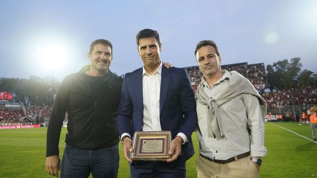 Sebastián Domínguez muestra la plaqueta entregada por el Mago Capria y el vice de Newells Daniel Asturzzi.