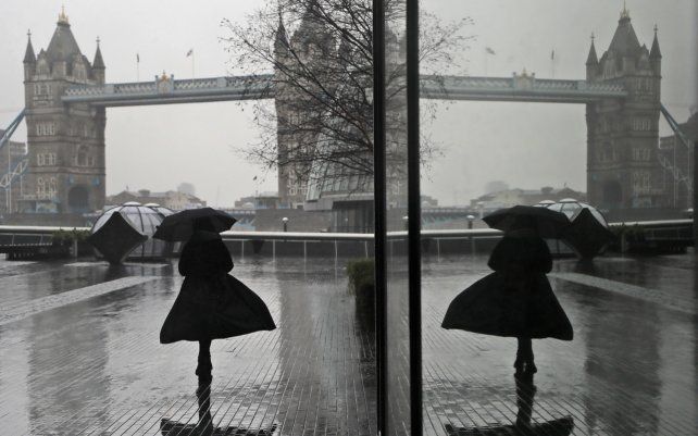 El reflejo de una mujer en una ventana desafiando el viento y la lluvia, mientras camina hacia el Puente de Londres.