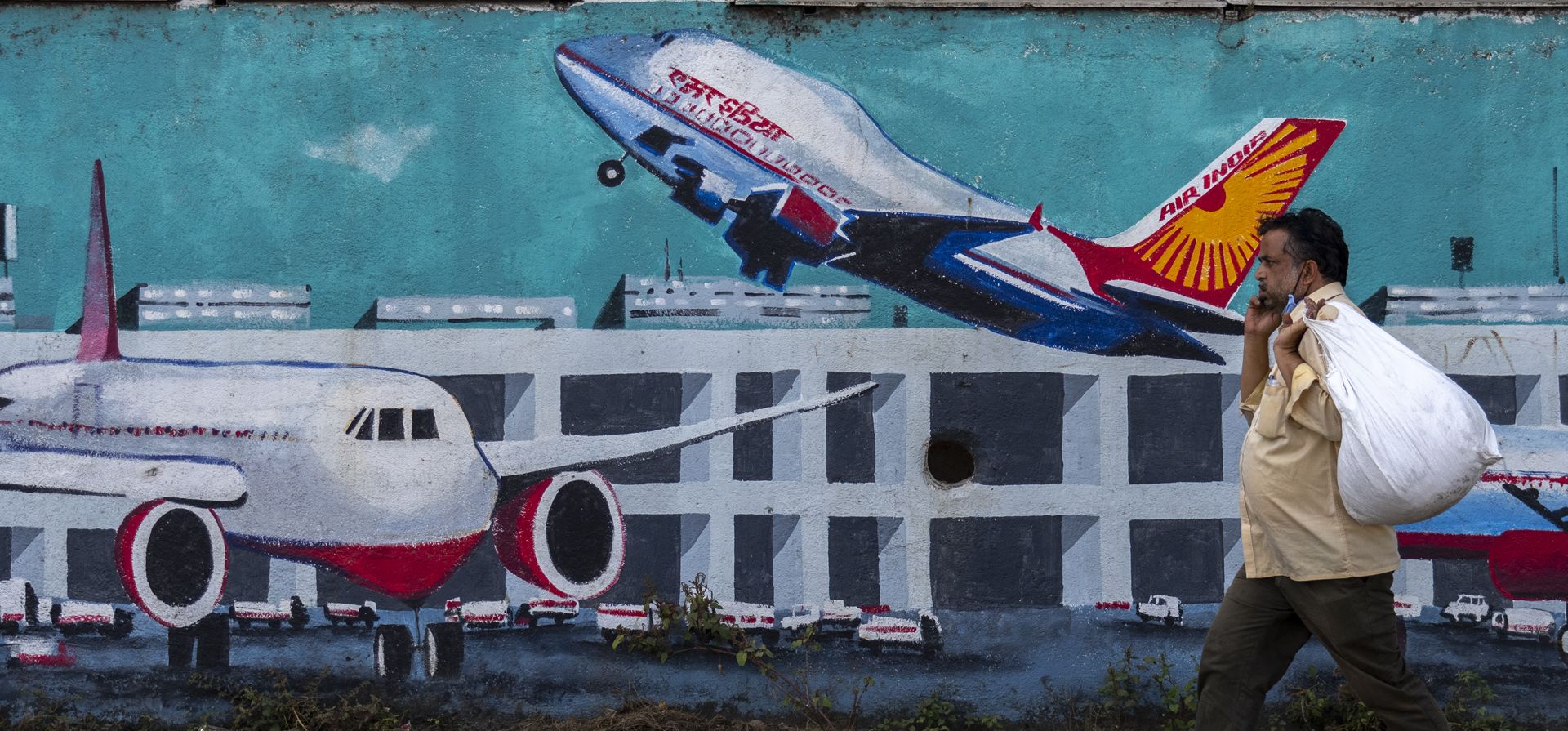 Una persona que habla por teléfono pasa frente a una pared pintada con aviones de Air India en Mumbai, India, el jueves 27 de enero de 2022. Tata Sons, el conglomerado más antiguo y más grande de India, recuperó el jueves la propiedad de la deuda del país. la cargada aerolínea nacional Air India que lanzó hace décadas pero que fue absorbida por el gobierno.