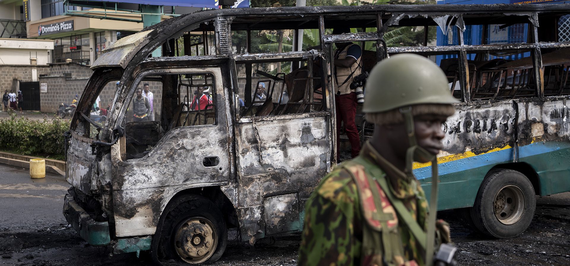 Un policía pasa junto a un minibús que fue incendiado y sus pasajeros robados durante los enfrentamientos cerca del barrio marginal de Kibera en la capital Nairobi, Kenia, el martes 2 de mayo de 2023.  (Foto AP/Ben Curtis)