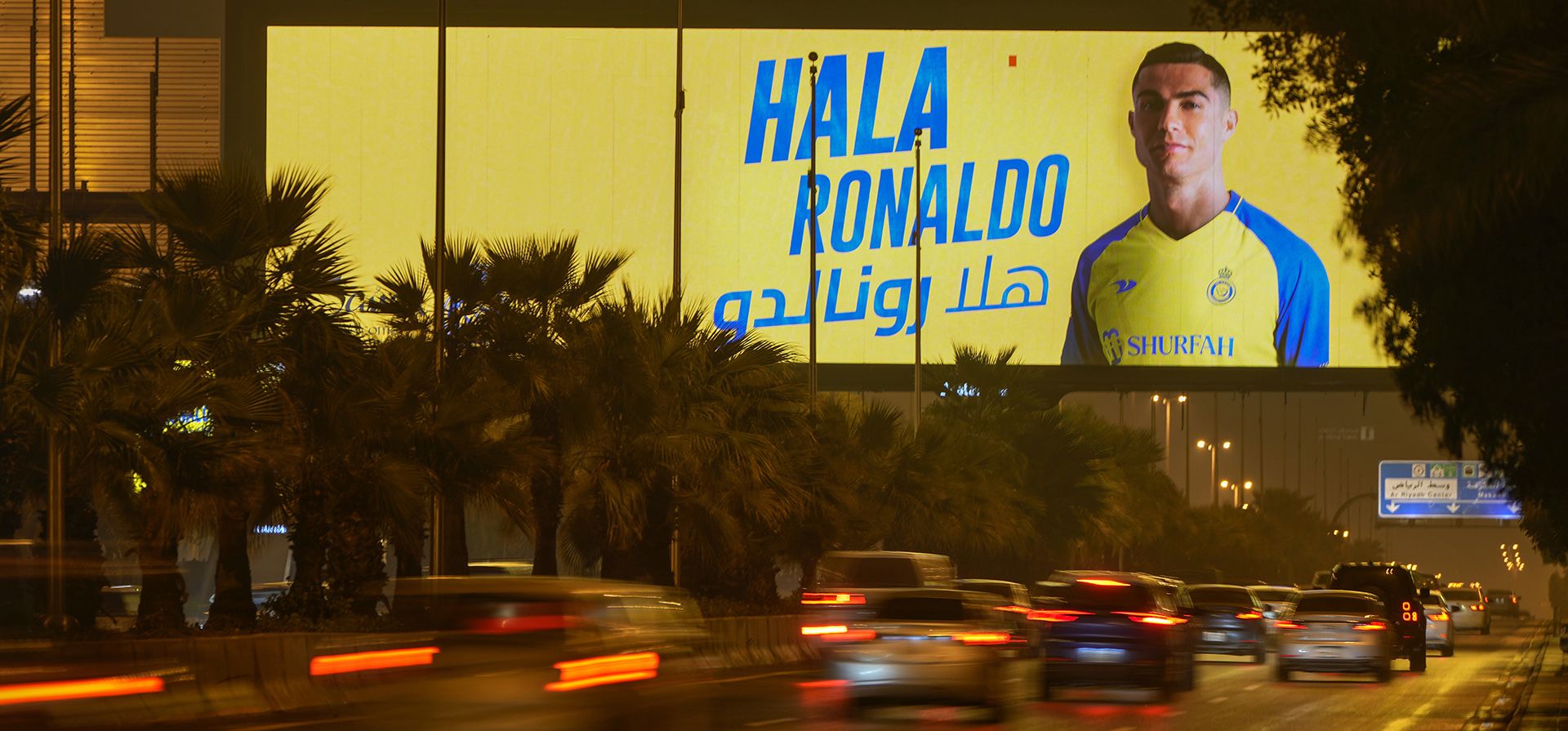 Vehículos pasan por debajo de una valla publicitaria que muestra a Cristiano Ronaldo con la palabra árabe