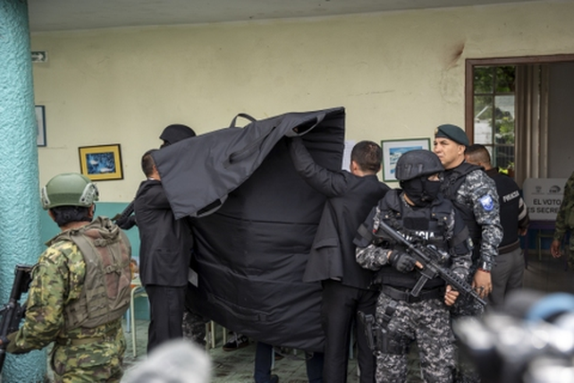 Christian Zurita, el candidato que reemplazó al asesinado Fernando Villavicencio, completamente tapado por un escudo antibalas y una fila de custodios frente a su mesa de votación.