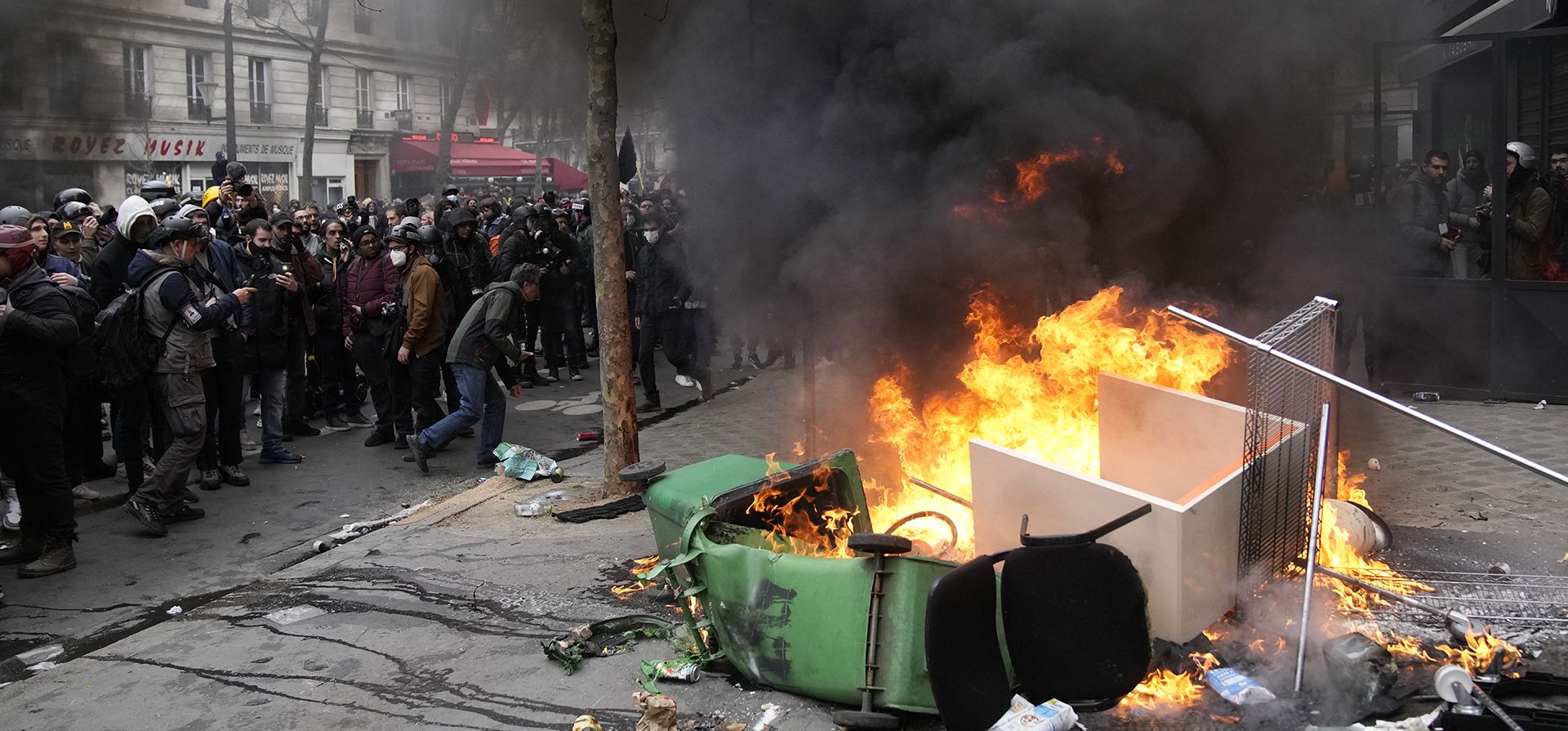 Manifestantes observan la quema de botes de basura durante una manifestación el martes 28 de marzo de 2023 en París. Es la ronda más reciente de manifestaciones y huelgas en todo el país contra las impopulares reformas de las pensiones y la campaña del presidente Emmanuel Macron para aumentar la edad legal de jubilación en Francia de 62 a 64 años. (AP Photo/Christophe Ena)