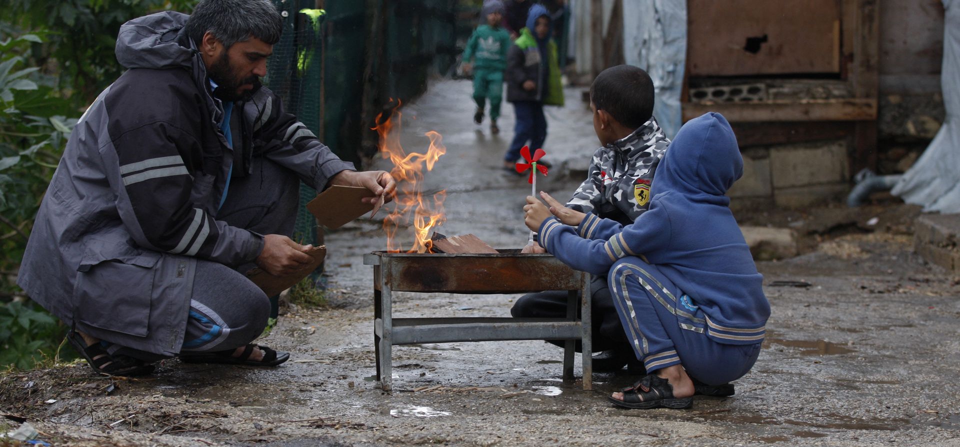 Una familia siria desplazada se calienta alrededor de una fogata en un campo de refugiados en la ciudad portuaria sureña de Sidón, Líbano, el miércoles 19 de enero de 2022. Una tormenta de nieve en el Medio Oriente ha dejado a muchos libaneses y sirios luchando por encontrar formas de sobrevivir.