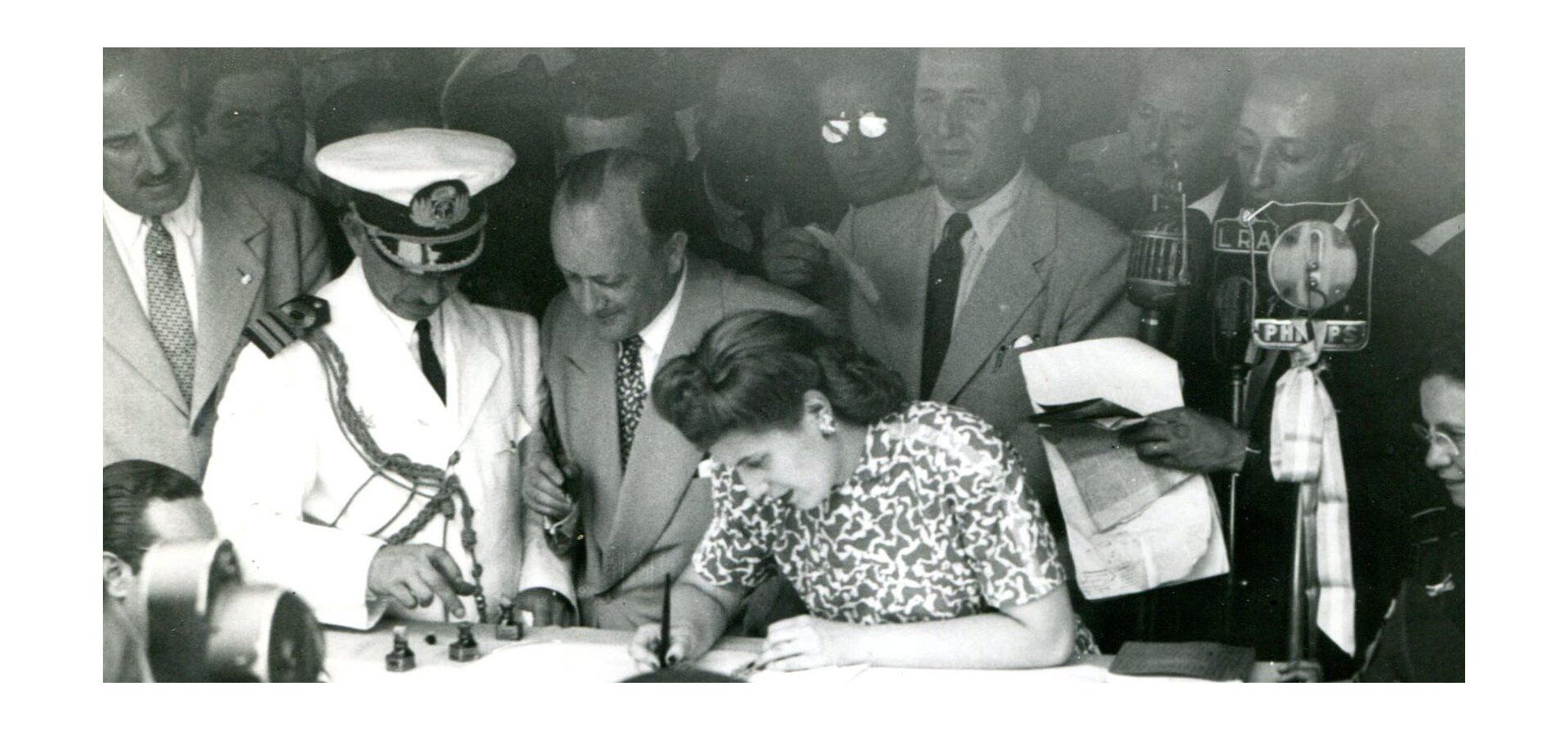 Eva Duarte firmando un pergamino en el Mercado de Hacienda, atrás Juan Perón, enero 1947.