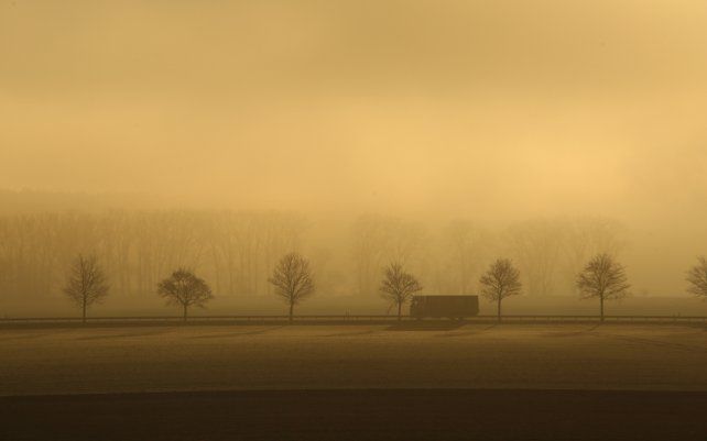 Un camión circula por una carretera durante un amanecer con intensa niebla cerca de Blankenburg, Alemania.