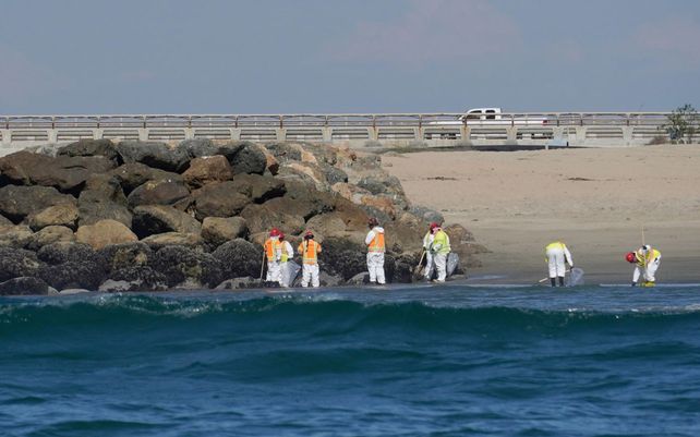 Equipos de limpieza caminan por la playa inspeccionando áreas y recuperan los escombros del derrame de petróleo depositados en Huntington Beach, California. Un derrame de petróleo envió hasta 126,000 galones de crudo pesado al océano.