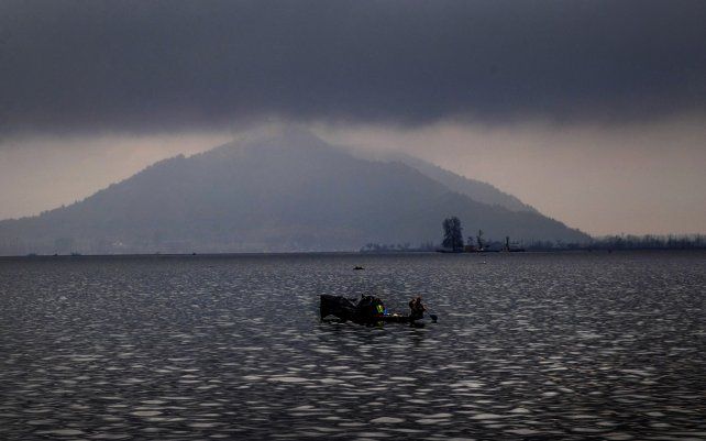 Un pescador rema su bote bajo las lluvias en el lago Dal en las afueras de Srinagar, Cachemira controlada por India.