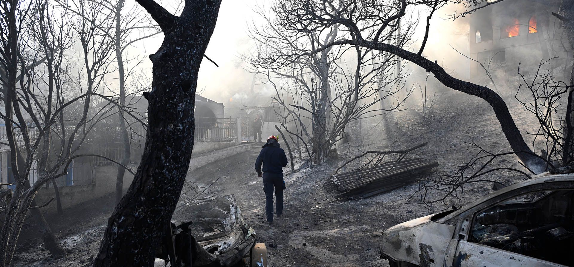 Un bombero camina por una zona quemada mientras las llamas envuelven una casa durante un incendio forestal en la isla de Salamina, al oeste de Atenas, Grecia, el domingo 16 de agosto de 2026. (Foto AP/Michael Varaklas)
