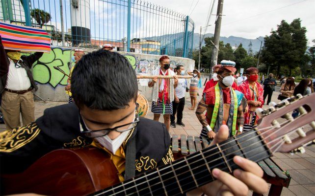 Un músico toca la guitarra junto a indígenas Tsachila que esperan afuera de la Asamblea Nacional el inicio de la ceremonia de inauguración del presidente electo Guillermo Lasso en Quito, Ecuador.