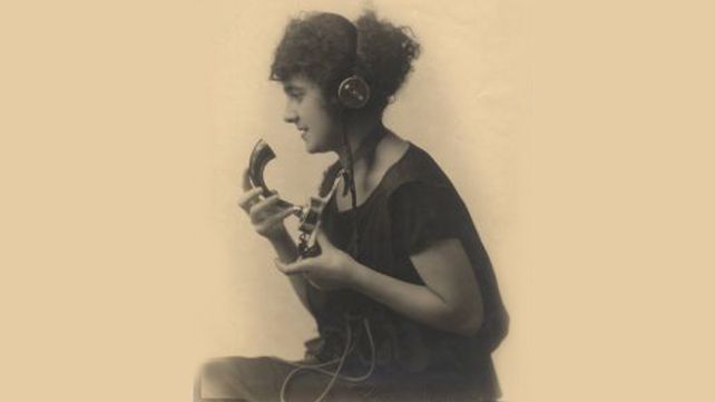 Una mujer habla con una antiguo aparato telefónico a fines del siglo XIX.