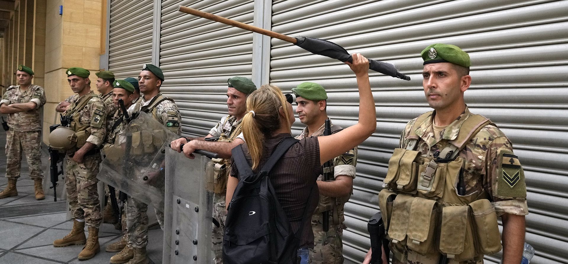 Un cliente de un banco golpea las paredes de metal de un banco mientras soldados del ejército montan guardia cerca del parlamento del Líbano durante una protesta contra un proyecto de ley de controles de capital que los manifestantes dijeron que restringiría aún más sus ahorros atrapados en los bancos, en Beirut, Líbano, el martes 30 de agosto de 2022.