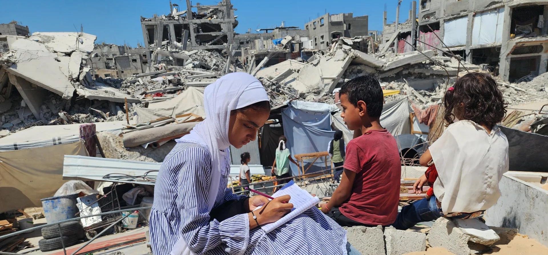 Los estudiantes hacen los deberes después de las clases en su escuela de campaña, construida sobre los escombros de la casa destruida del profesor, Khan Younis, Gaza. Fotografía: Anadolu/Getty Images Los estudiantes hacen los deberes después de las clases en su escuela de campaña, construida sobre los escombros de la casa destruida del profesor, Khan Younis, Gaza. Fotografía: Anadolu/Getty Images