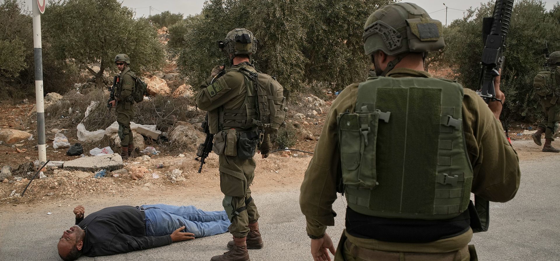 Soldados israelíes junto a un palestino herido que yace en una carretera después de que los soldados le dispararan tras un ataque de colonos contra palestinos que cosechaban aceitunas en la aldea ocupada de Abu Falah en Cisjordania, el viernes 16 de octubre de 2026. (Foto AP/Leo Correa)
