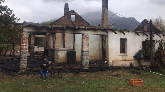 Un niño se muestra sentado delante de las ruinas de su casa