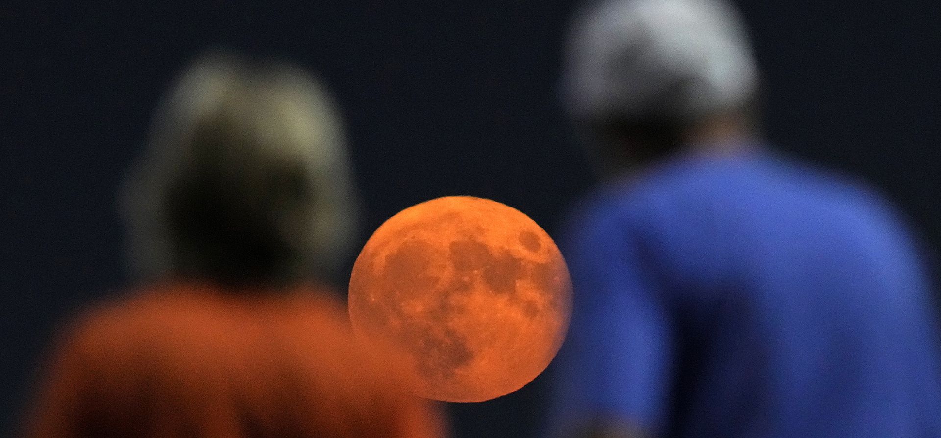 La gente observa desde el piso superior un partido de béisbol entre los Reales de Kansas City y los Piratas de Pittsburgh mientras la luna sale a lo lejos el miércoles 30 de agosto de 2023 en Kansas City, Missouri. (Foto AP/Charlie Riedel)