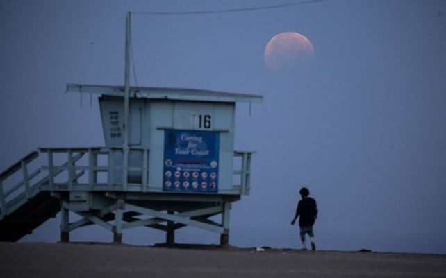 Una mujer observa cómo la luna llena se pone sobre la playa de Santa Mónica en California