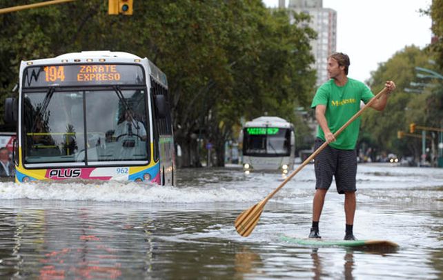 Un joven recorre una avenida porteña navegando en una tabla y remando. 2) Un vecino navega por su barrio en un bote inflable.