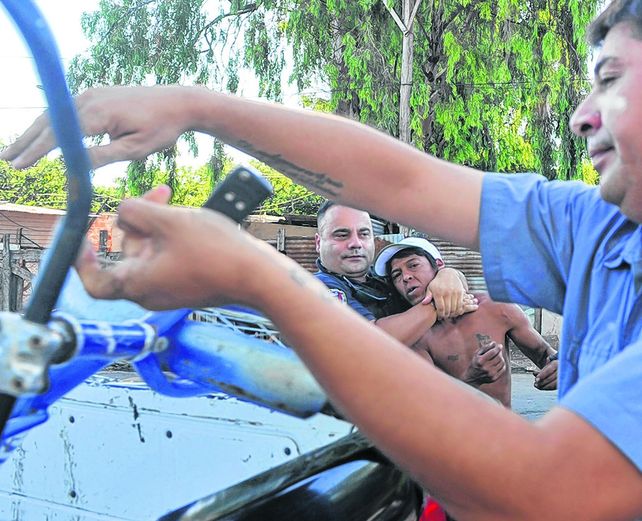 detención. Un policía detiene a un hombre que pasaba por el lugar en bicicleta. La policía insultó a la prensa.
