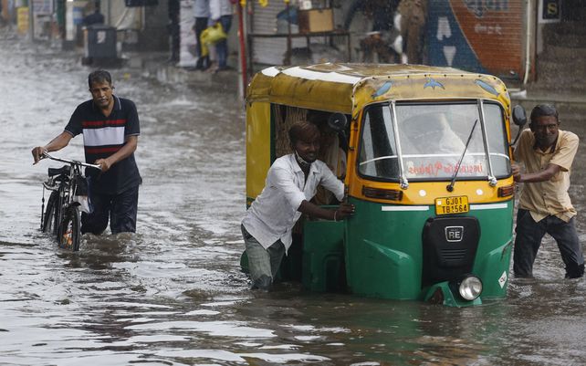 La gente empuja un shaw junto a una carretera inundada durante las lluvias en Ahmedabad